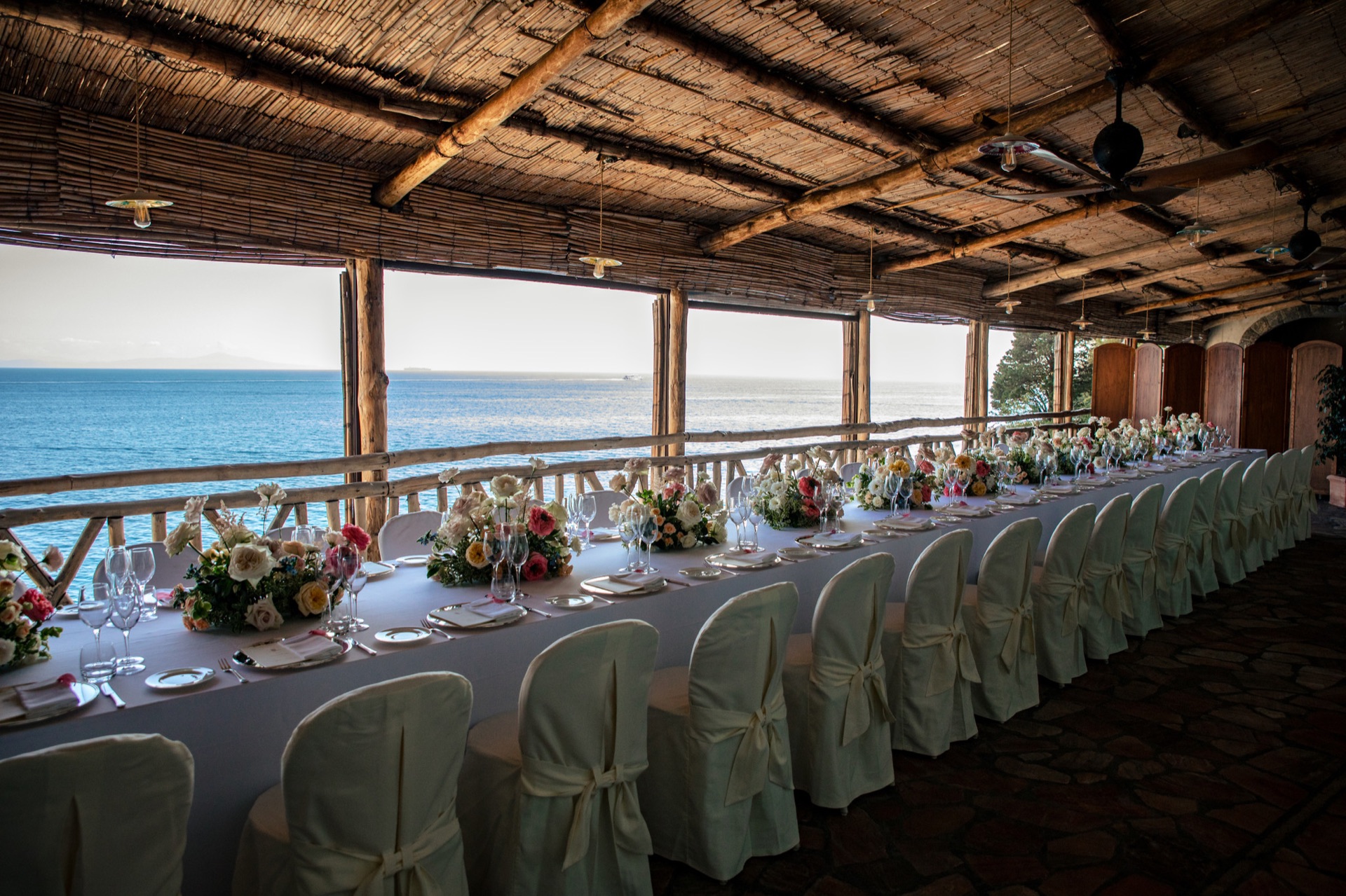 A long wedding table with pink and white flowers overlooking the Amalfi Coast
