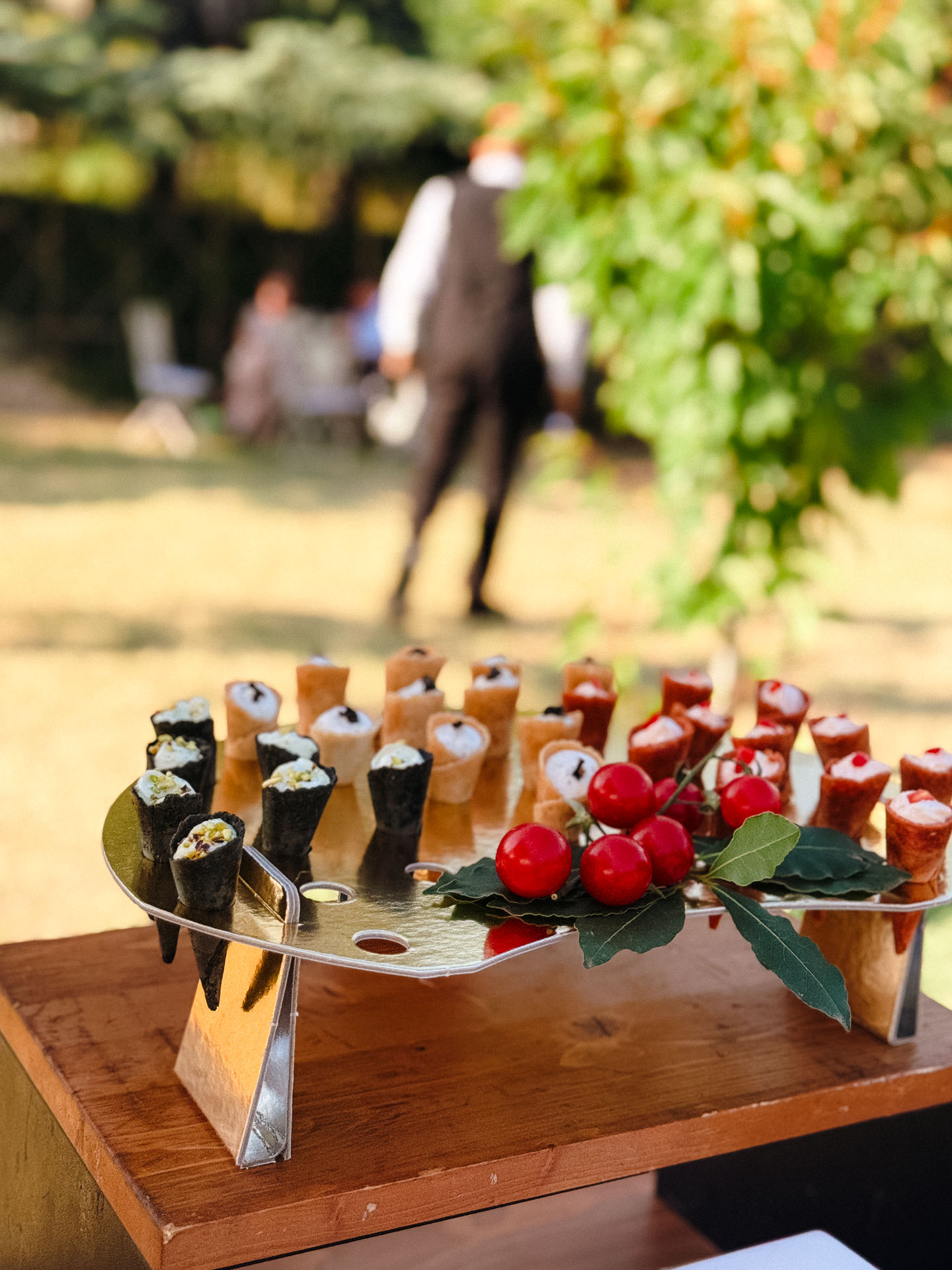 Assorted bite-sized hors d'oeuvres on a metal stand outdoors, including seaweed-wrapped rolls and red berries with leaves garnish.