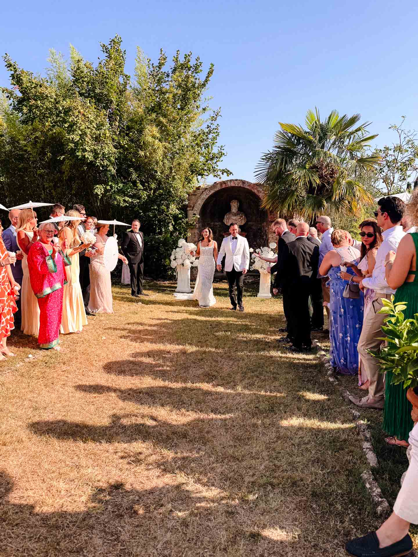 Bride and groom walk down a grassy aisle lined with guests at an outdoor wedding.