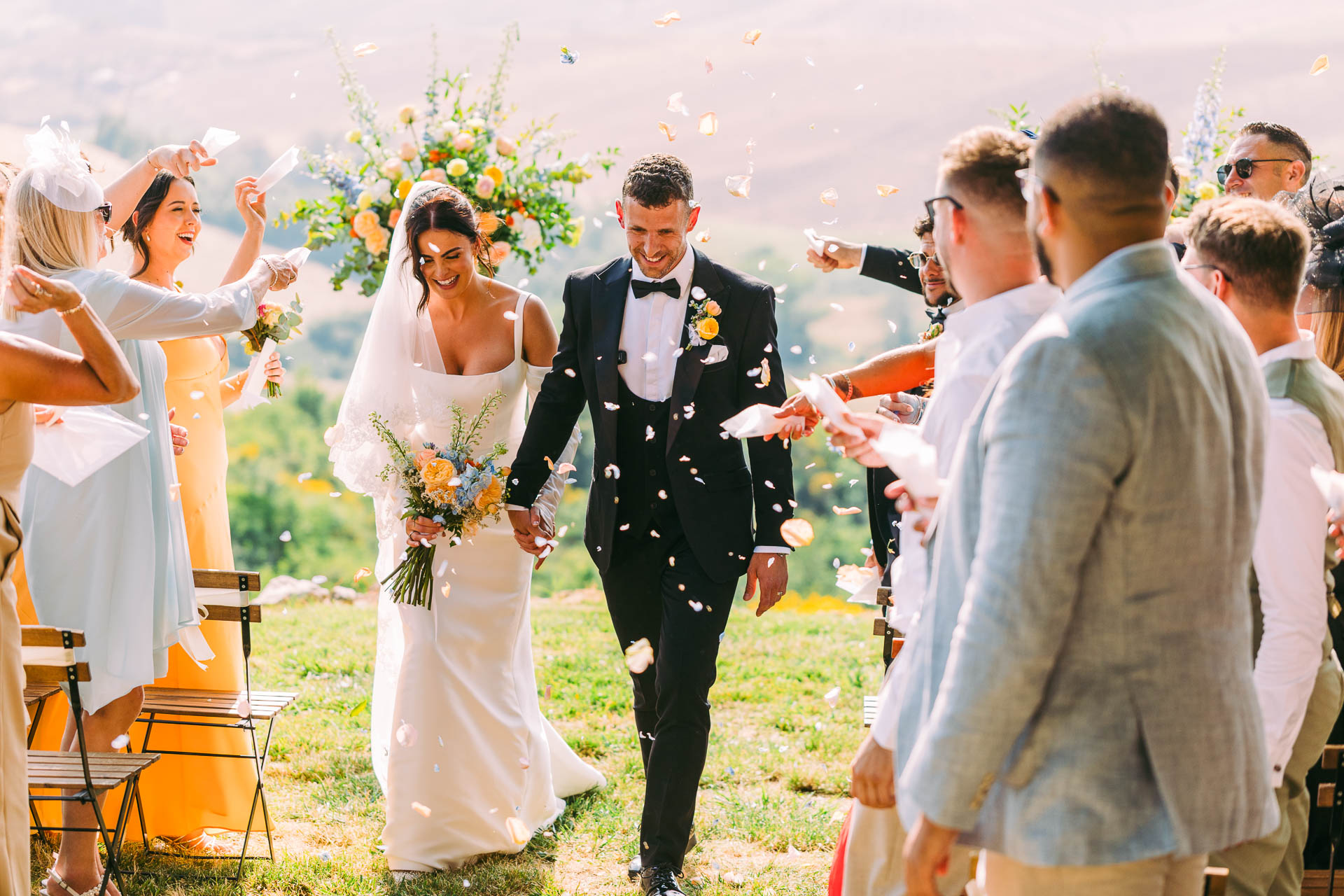 Nikita and Jason walk through their smiling guests under falling petals